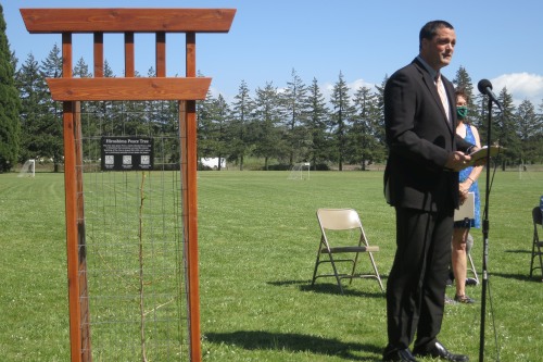 Principal Peter Henning speaking at microphone beside Peace tree in protective fence